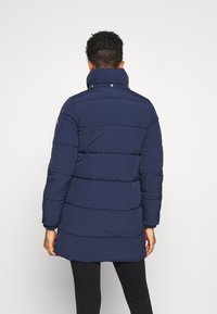 Marinblå puffjacka med hög krage, med quiltade sektioner, tryckknappar och långa ärmar. Snygg textur och mitt på låret längd.