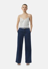 Silver sequined camisole with thin straps, paired with high-waisted dark blue wide-leg jeans and silver block-heel sandals.