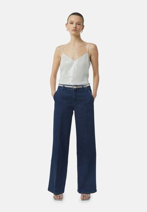 Silver sequined camisole with thin straps, paired with high-waisted dark blue wide-leg jeans and silver block-heel sandals.