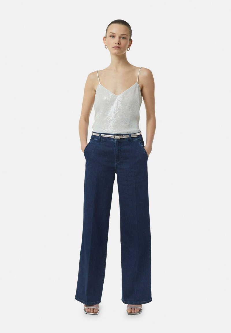 Silver sequined camisole with thin straps, paired with high-waisted dark blue wide-leg jeans and silver block-heel sandals.
