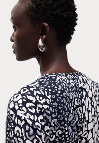 Námořnický top s bílým abstraktním leopardím vzorem, s kulatým výstřihem. Velké stříbrné slzičkové náušnice dotvářejí vzhled.