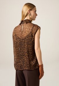 Top in stampa leopardata marrone trasparente con collo alto e chiusura con bottoni sul retro, abbinato a guanti in pelle marrone.