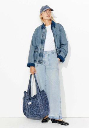 Veste en jean à délavage clair, assortie à un pantalon en jean large et clair. Sac fourre-tout à imprimé léopard bleu et chaussures noires avec des pois blancs.