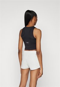 Schwarzes, figurbetontes Sportoberteil mit gekrümmten Nähten und Logodetail, kombiniert mit hellgrauen Shorts mit elastischem Bund und umgeschlagenem Saum.