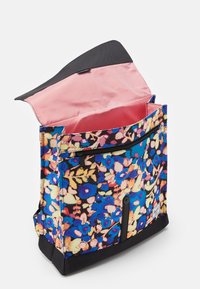 Sac à dos à motif floral en tissu avec une base noire. Intérieur rayé rouge et blanc, comprenant une poche avant avec zip et un rabat supérieur.