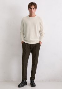 Sweter w kolorze kremowym, lekka dzianina, okrągły dekolt; ciemnozielone spodnie, dopasowany krój; czarne sznurowane buty o gładkim wykończeniu.