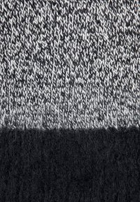 Tissu tricoté à motif noir et blanc, présentant une texture douce avec un dessus lisse et un bord inférieur noir duveteux.