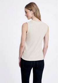 Top smanicato beige a coste con scollatura rotonda, texture liscia e design aderente, abbinato a jeans in denim neri.