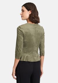 Oliwkowa, sztuczna zamszowa kurtka z rękawami 3/4, peplum u dołu i bocznymi rozporkami. Prosty design, dopasowana sylwetka i gładka tekstura.