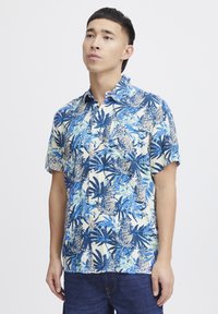 Camicia a maniche corte blu e crema con motivo tropicale di ananas e foglie, chiusura con bottoni sul davanti e dettaglio della tasca sul petto.