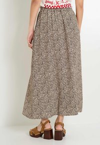 Larga falda plisada en beige con manchas de leopardo negras. Llevada con sandalias de plataforma gruesa marrones, con tachuelas doradas y correas ajustables.