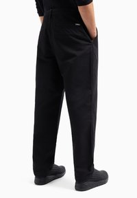 Pantaloni in cotone neri con vestibilità rilassata, tasche posteriori e tasche laterali. Abbinati a sneaker nere, che mostrano una texture liscia.