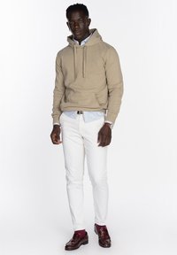 Sudadera con capucha beige con cordones, camiseta blanca debajo, pantalones blancos y mocasines burdeos. Cuenta con un bolsillo tipo canguro y una marca sutil.