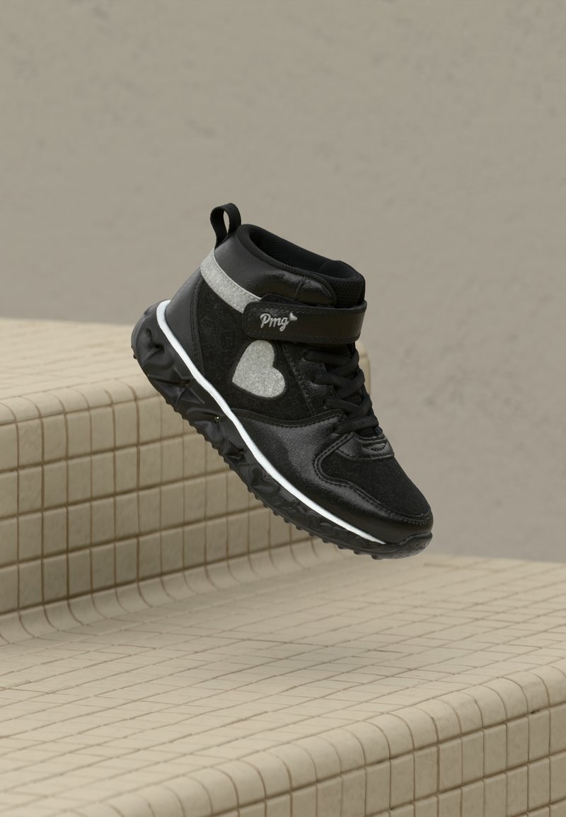 Mustad musta värvi kõrgete sportlike tossudega, millel on südame motiiv, takjakinnitus ja tekstureeritud tald, mis hõljub beeži plaaditud astmete kohal.