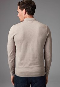 Beige gestrickter Pullover mit langen Ärmeln, ribbeligem Kragen und Saum, mit glatter Textur und tailliertem Design, von hinten gezeigt.