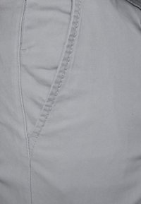 Szare bawełniane spodnie o gładkiej fakturze, z ukośnymi przednimi kieszeniami i kontrastującym przeszyciem wzdłuż szwów.