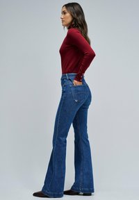 Maglietta rossa aderente a maniche lunghe abbinata a jeans a zampa d'elefante blu a vita alta, che mostrano una classica texture denim e tasche strutturate.