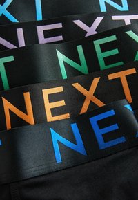 Ropa interior negra con cinturas elásticas coloridas que muestran la palabra "NEXT" en azul, verde, púrpura y naranja. Textura suave, diseño plano.