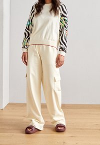 Pull en maille crème avec manches à imprimé zèbre et accents floraux, associé à un pantalon cargo crème et des sandales marron à enfiler.