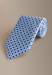 Lyseblåt slips med et geometrisk mønster af vekslende mørkeblå firkanter og diamanter med røde accenter. Glat tekstur, rullet pænt sammen.