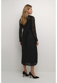 Svart spetsklänning med långa ärmar, blommönster, åtdragen midja och längd till mitten av vadbenet. Kombinerad med svarta stiletto klackar, slät textur.