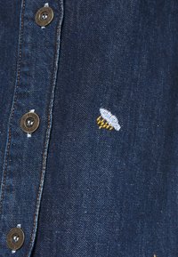 Denim shirt with a deep blue color, featuring silver metallic buttons and a small embroidered graphic of a flying saucer in blue and yellow.