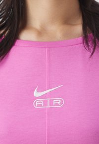 Rosa idrottstopp med rund krage, med en vit Nike swoosh-logotyp och texten "AIR" broderad på framsidan. Mjuk tygstruktur.