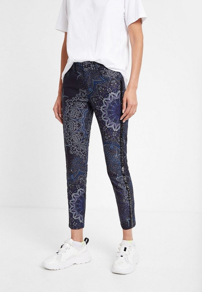 Pantalon skinny bleu marine avec des motifs complexes bleu et blanc. Doté d'une texture lisse et d'une ceinture élastique, associé à des baskets blanches.