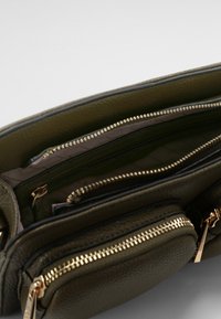 Olijfgroen leren handtas met gouden hardware, voorzien van meerdere ritscompartimenten en een gestructureerde buitenkant.