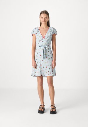 Abito azzurro chiaro con stampa floreale, scollo a V, maniche a sbuffo e fiocco in vita. Indossato con sandali neri con cinturini.