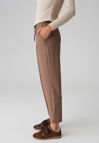 Pantaloni marroni, affusolati, con elastico in vita e tasche laterali, abbinati a sneaker marroni scuri. Tessuto morbido con una texture liscia.