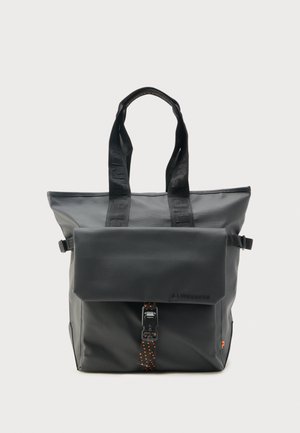 Sac cabas noir avec poignées supérieures, poche avant à rabat sécurisée par une boucle et sangle à pois orange, design minimaliste sur fond uni.