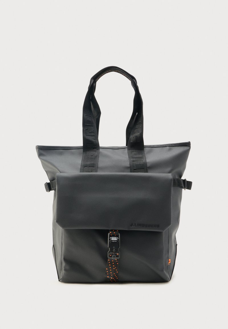 Sac cabas noir avec poignées supérieures, poche avant à rabat sécurisée par une boucle et sangle à pois orange, design minimaliste sur fond uni.