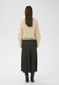 Pull en tricot beige à manches longues, assorti à une jupe noire à pois crème, et des bottes noires montant jusqu'aux genoux.