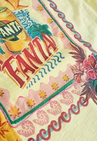 Tissu lumineux avec logo Fanta style vintage, palmiers, étoiles, vagues, motifs coquillages et broderie fleur d’hibiscus perlée rose.
