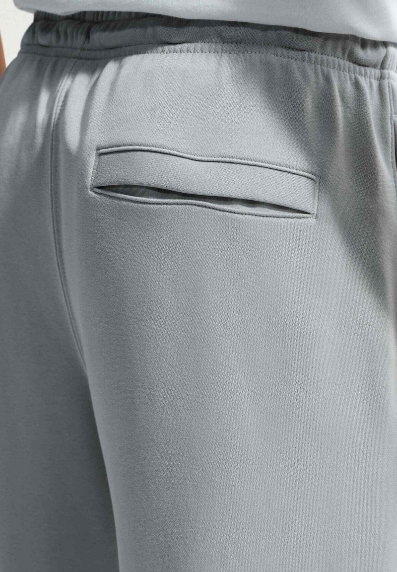 Lysegrå sweatpants med elastisk linning og en vandret skrålomme på højre bagside.