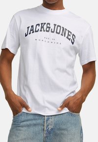 Weißes Baumwoll-T-Shirt mit einem auffälligen dunkelblauen Logo "JACK&JONES" über der Brust, Gründungsjahr 1990 und lässiger Schnitt.