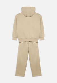 Σετ μπεζ βαμβακερή μπλούζα με κουκούλα και αντίστοιχο παντελόνι φόρμας. Σχεδίαση με κουκούλα, ριμπ μανσέτες και ζώνη μέσης. Λείο ύφασμα, άνετη εφαρμογή, χωρίς εμφανές λογότυπο.
