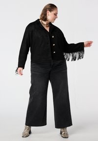 Zwarte suède jas met franjes aan de mouwen en gouden knopen. Gecombineerd met donkerdere wijde jeans en enkellaarsjes met slangenprint.