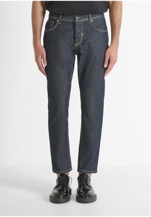 Dark blue denim jeans with yellow stitching, five pockets, and a straight leg design, paired with black shiny dress shoes.