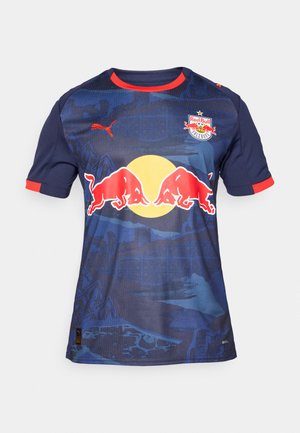 Jersey de manga corta azul con acentos rojos, un logo central con dos toros cargando y un gráfico de sol amarillo sobre un fondo texturizado de montaña.