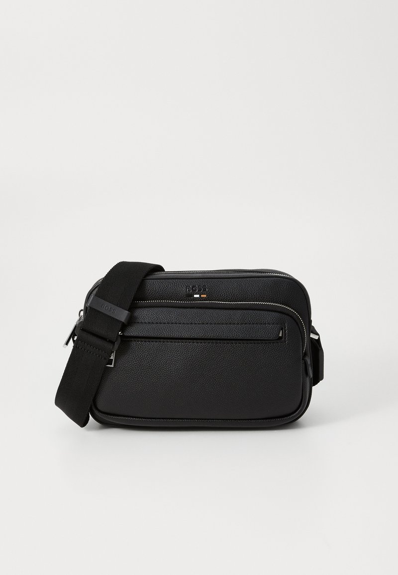 Compact black crossbody bag with textured leather, front zipper pocket, adjustable strap, and subtle brand logo on the front.