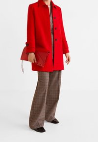 Rød uldfrakke med lige snit, med krave og knaplukning. Sammenlignet med brune plaid-brede ben bukser og en rød clutch.