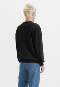 Felpa nera con scollo tondo, polsini e orlo a coste. Indossata sopra jeans in denim azzurro chiaro, che mostrano un fit rilassato e una morbida texture.