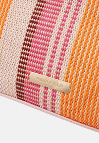 Kolorowa pleciona kopertówka z paskami w odcieniach różu, pomarańczu, beżu i brązu, z plakietką z logo w złotym odcieniu. Gładka faktura i kompaktowy kształt.