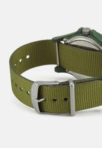 Timex-Uhr mit grünem Stoffarmband und silberner Schnalle, ausgestattet mit einer strukturierten Nylon-Webart und einem eckigen grünen Gehäuse.