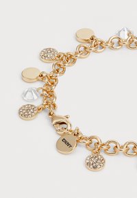 Pulsera de cadena en tono dorado con charm redondos y en forma de lágrima con acentos de cristal y un cierre de langosta. Incluye una etiqueta con el logo de DKNY.