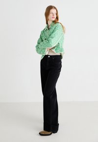 Giacca verde con motivo floreale e colletto leggero, foderata in crema, abbinata a jeans neri a gamba dritta e scarpe con tacco quadrato color beige.