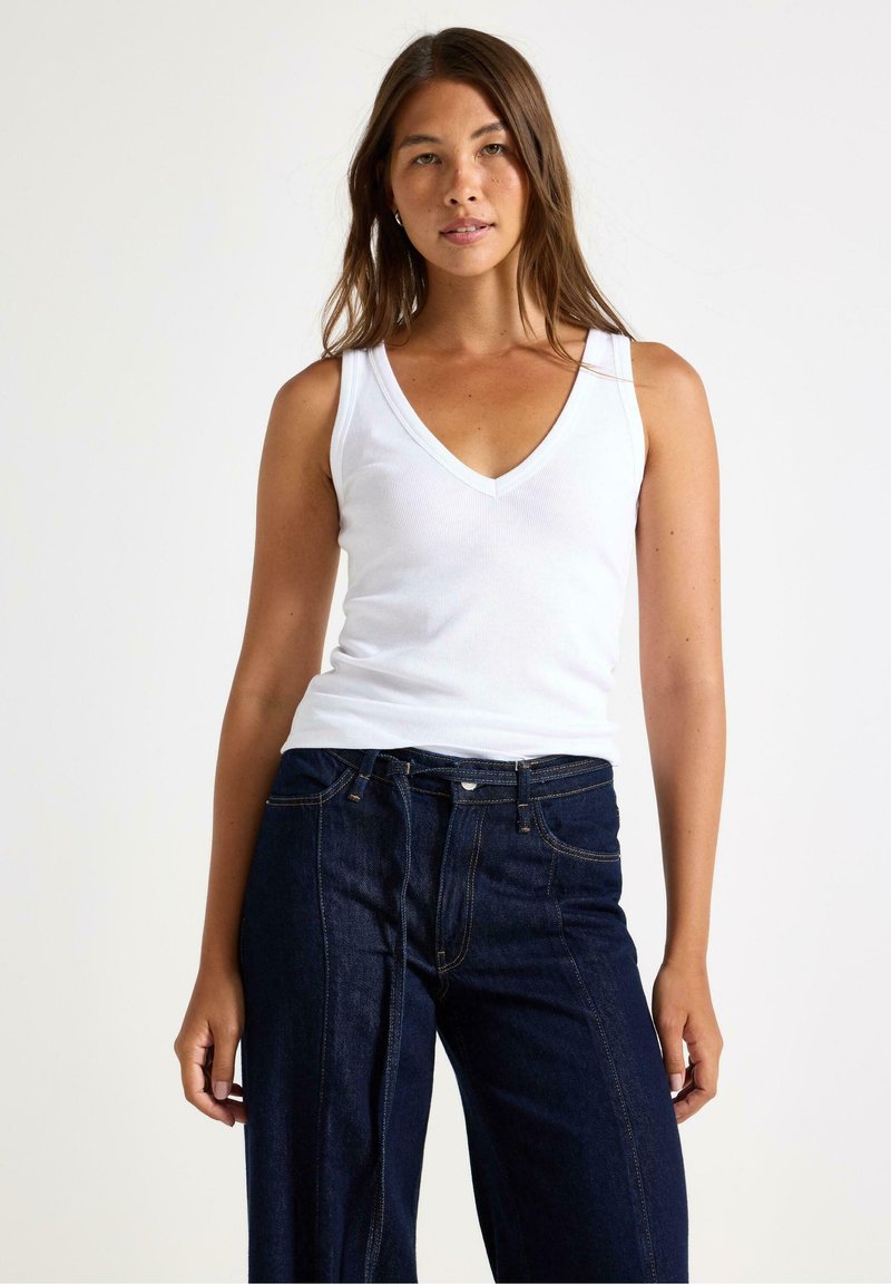 Hvid bomulds tanktop med v-hals, parret med mørkeblå vide jeans. Glat tekstur og simpelt design uden synlige mønstre.