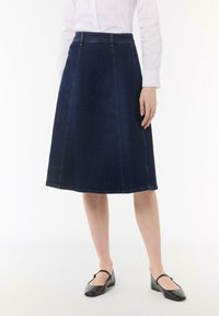 Dunkelblaue Denim-A-Linien-Rock mit hoher Taille, mit kontrastierender Naht und knielangem Saum. Getragen mit schwarzen Ballerinas.